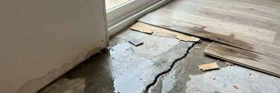 Water seeping up through a cracked slab under lifted flooring in a North Texas home