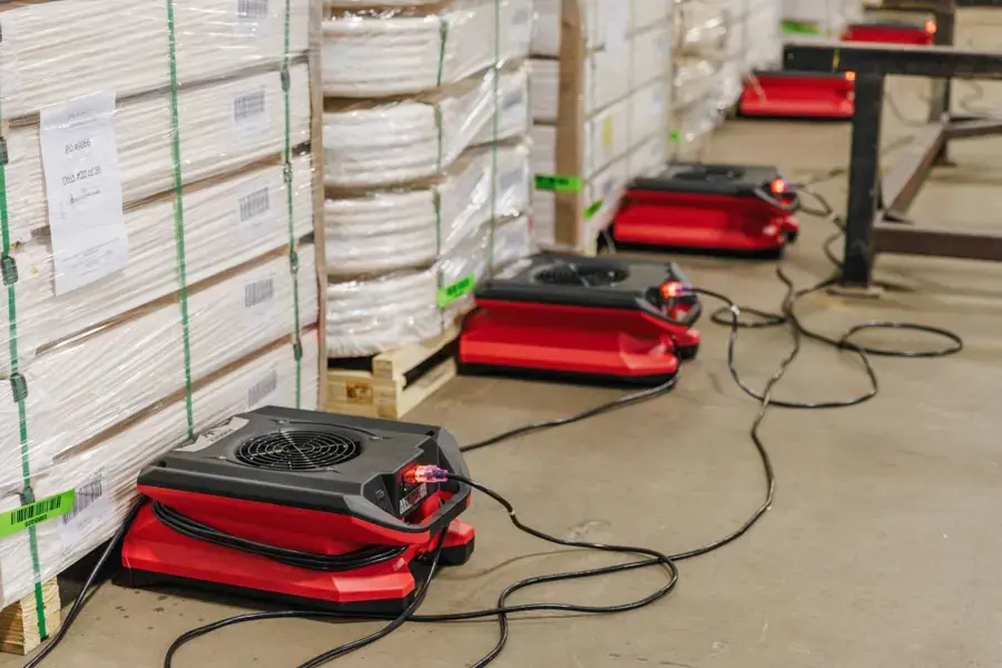 Air movers drying a warehouse floor between stacked inventory in Carrollton