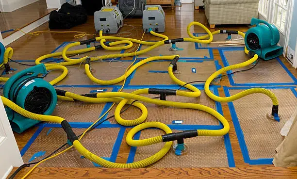 Hardwood floor drying panels and air movers taped over a wet wood floor